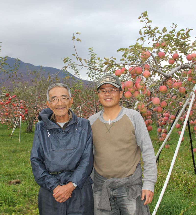 青森のリンゴ畑で木村秋則さんと著者の写真